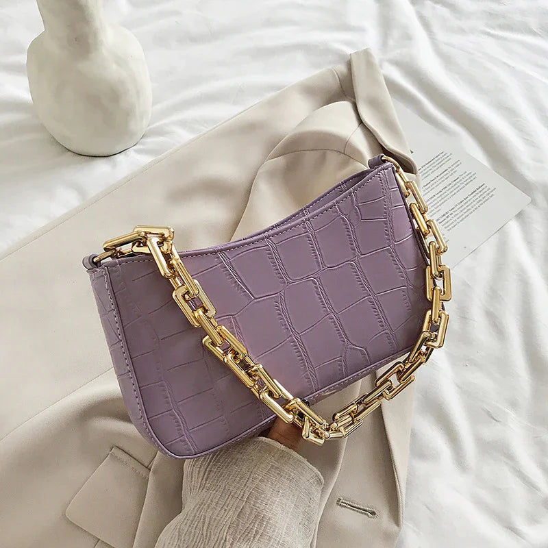 Lavender crocodile texture handbag with chunky gold chain strap on beige coat and white fabric