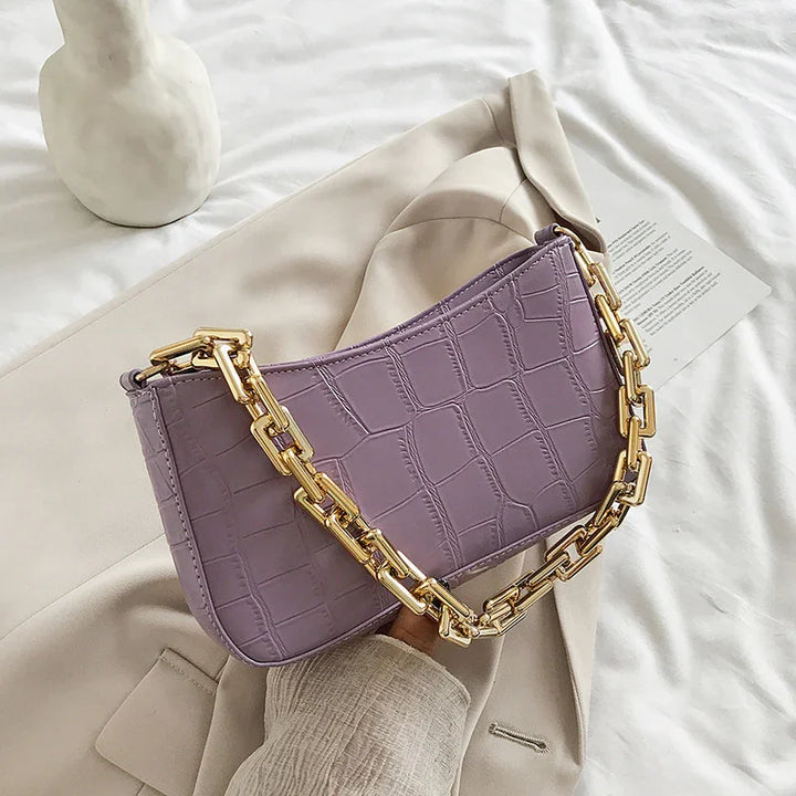 Lavender crocodile texture handbag with chunky gold chain strap on beige coat and white fabric