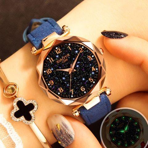 XIAOYA rose gold watch with starry black dial and blue strap on wrist with black and glittery nail art
