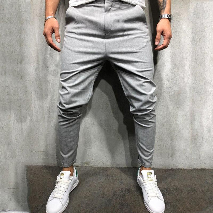 Man wearing slim-fit gray jogger pants and white sneakers against concrete wall