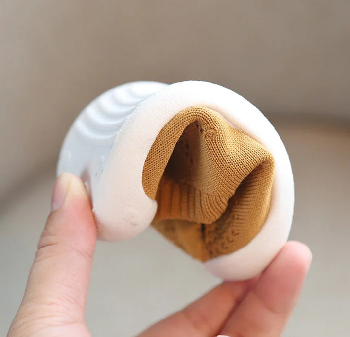 Hand holding a flexible white sole with a brown knitted fabric shoe upper, demonstrating bendability