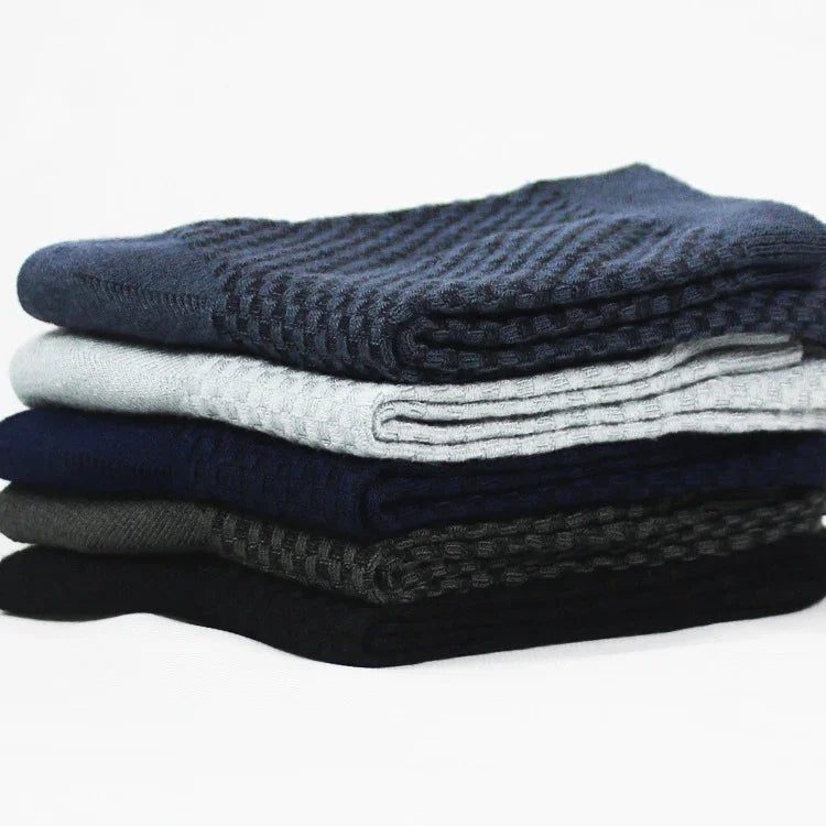 Stack of folded textured knit sweaters in black, gray, navy, and blue on white background