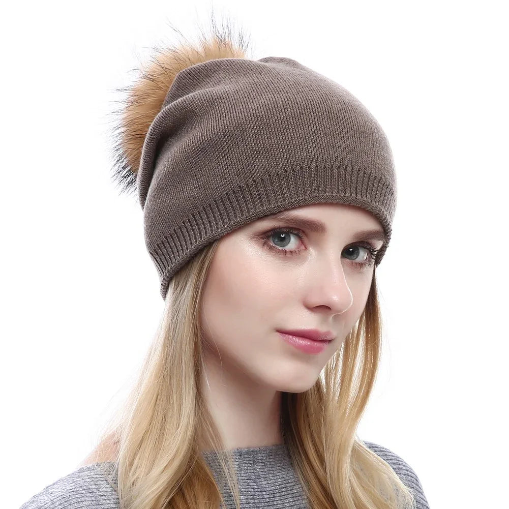 Woman wearing taupe knit winter beanie with brown faux fur pom-pom and gray sweater