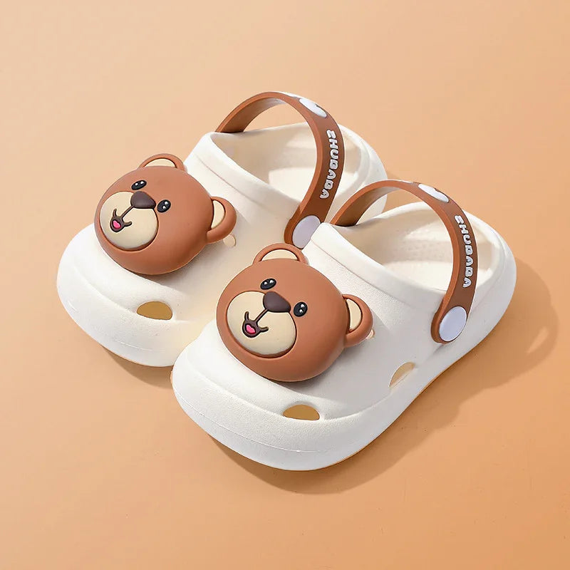 White kids clogs with brown bear face decoration and adjustable brown strap on beige background