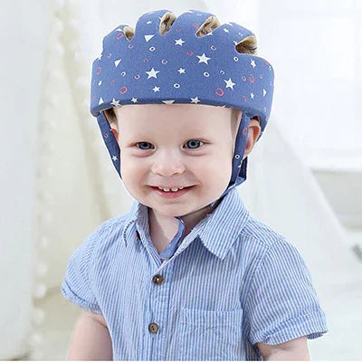 Smiling toddler wearing blue protective helmet with star and moon patterns, dressed in striped shirt