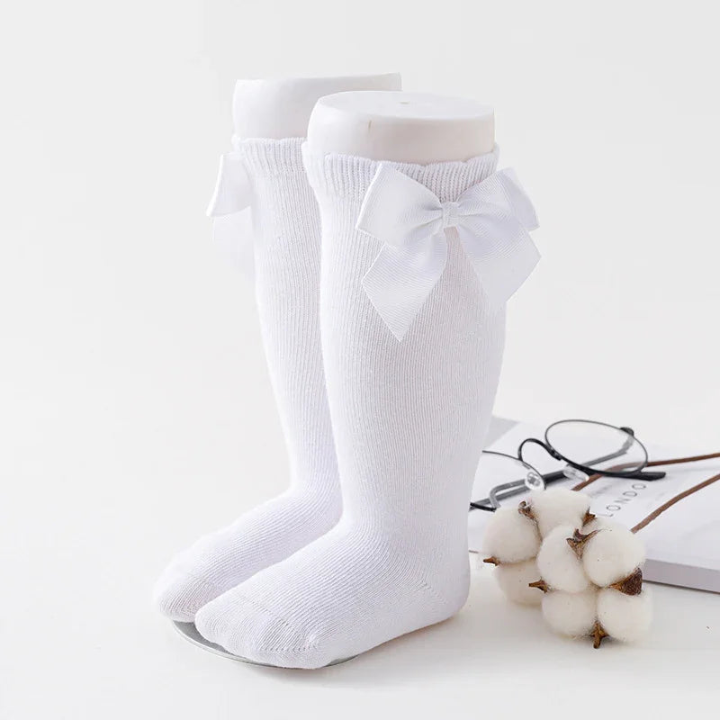 Pair of white knee-high baby socks with decorative bows on mannequin legs