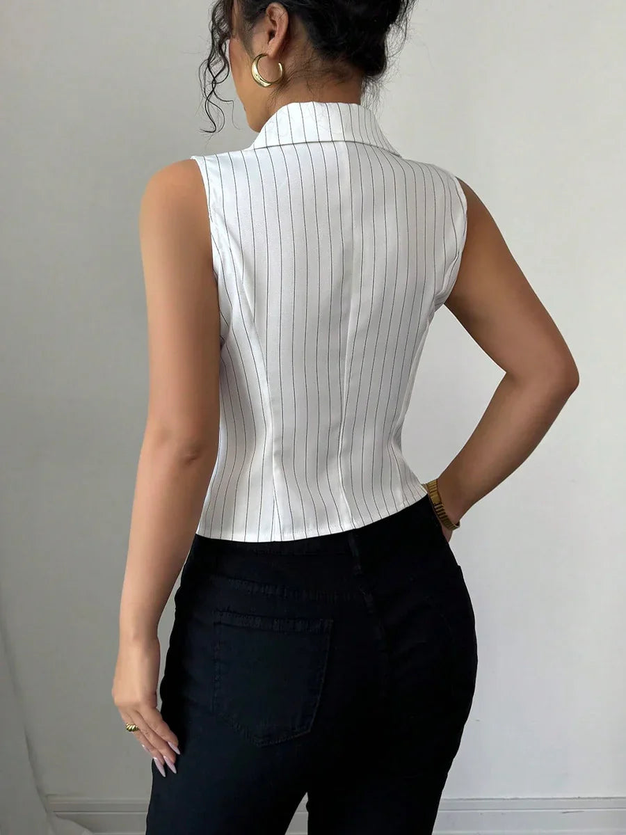 Woman wearing sleeveless white pinstripe top with collar and black pants, posing against plain background