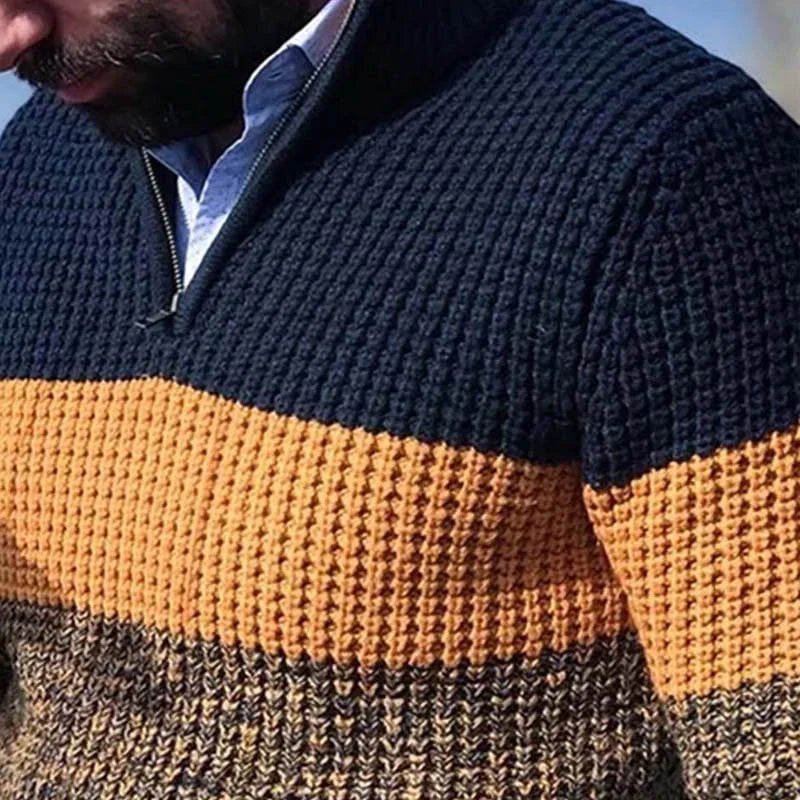 Close-up of a man wearing a textured knit sweater with navy, mustard yellow, and brown color blocks and a partially zipped collar