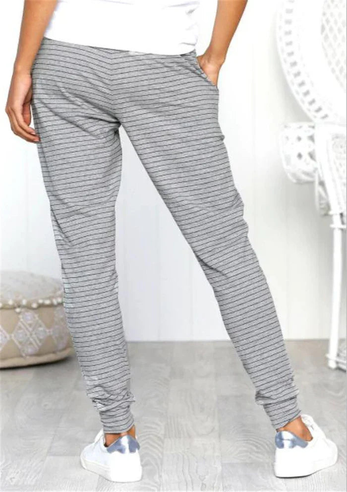 Person wearing gray striped jogger pants and white sneakers in a bright room with wooden floor