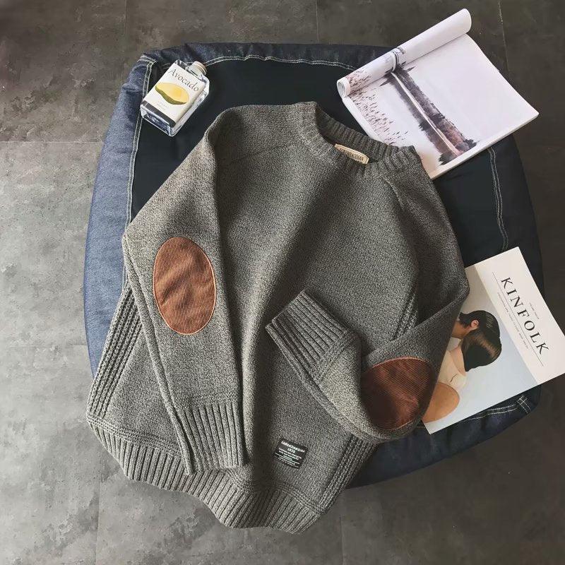 Gray knit sweater with brown elbow patches on a dark cushion, beside an avocado-scented bottle and open Kinfolk magazine