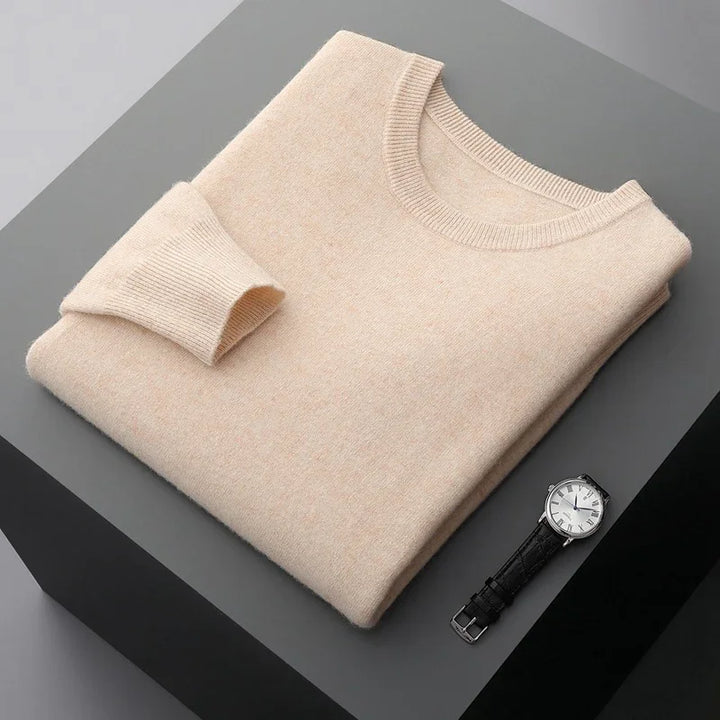 Folded beige crew neck sweater on gray surface with silver watch and black leather strap