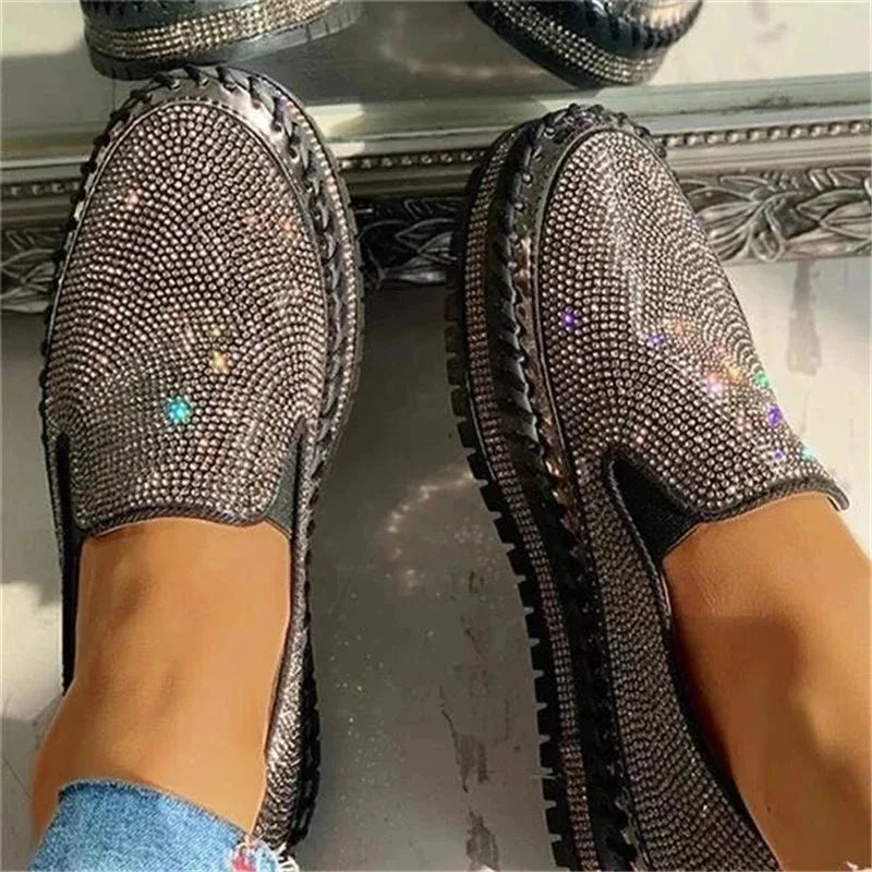 Sparkling silver rhinestone loafers with black soles and decorative stitching worn with blue jeans