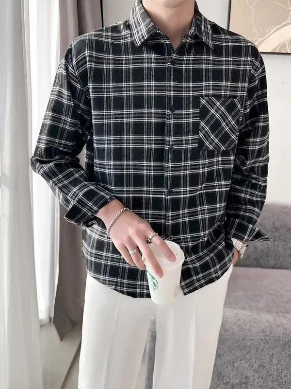 Man wearing black and white plaid long-sleeve shirt with front pocket and white pants holding a Starbucks cup indoors