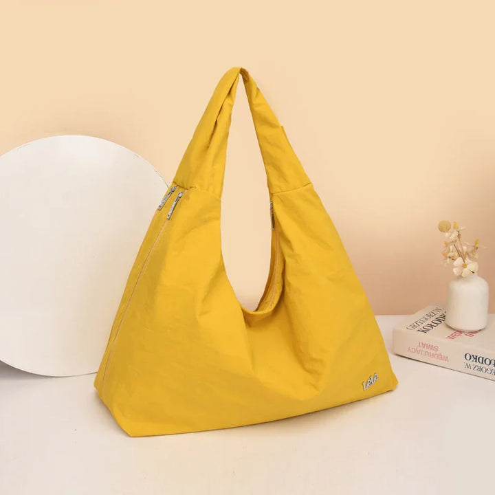 Yellow fabric tote bag with zipper side pockets on beige background with books and vase