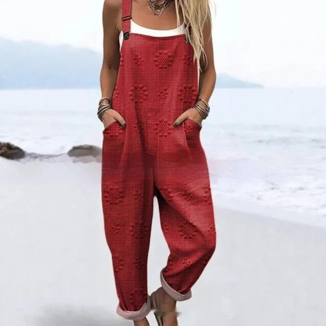 Woman wearing red floral textured overalls with rolled cuffs and white tank top on beach background