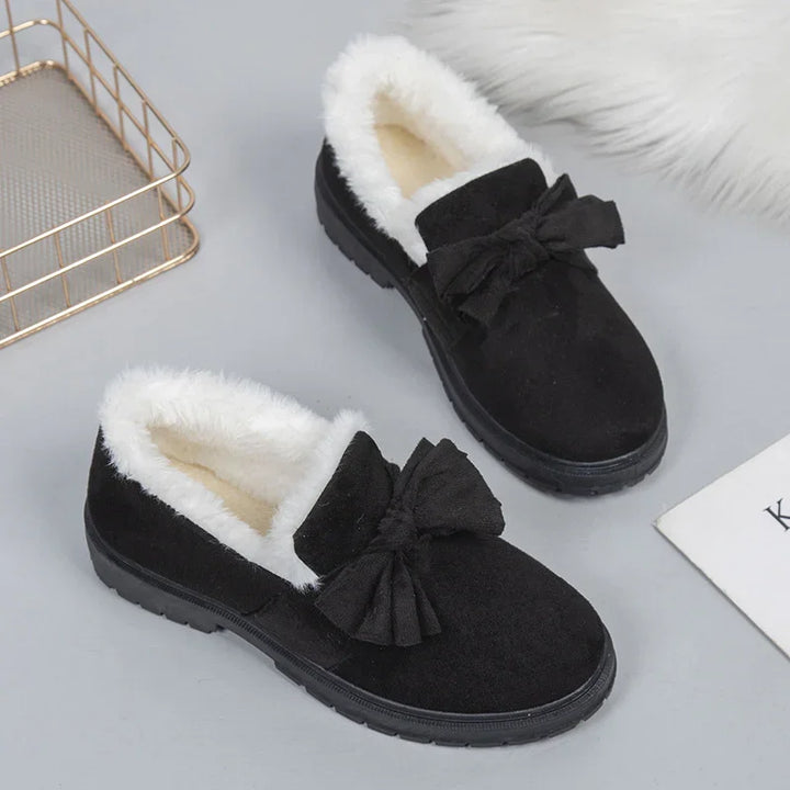 Black slip-on winter shoes with white fur lining and decorative bow on top