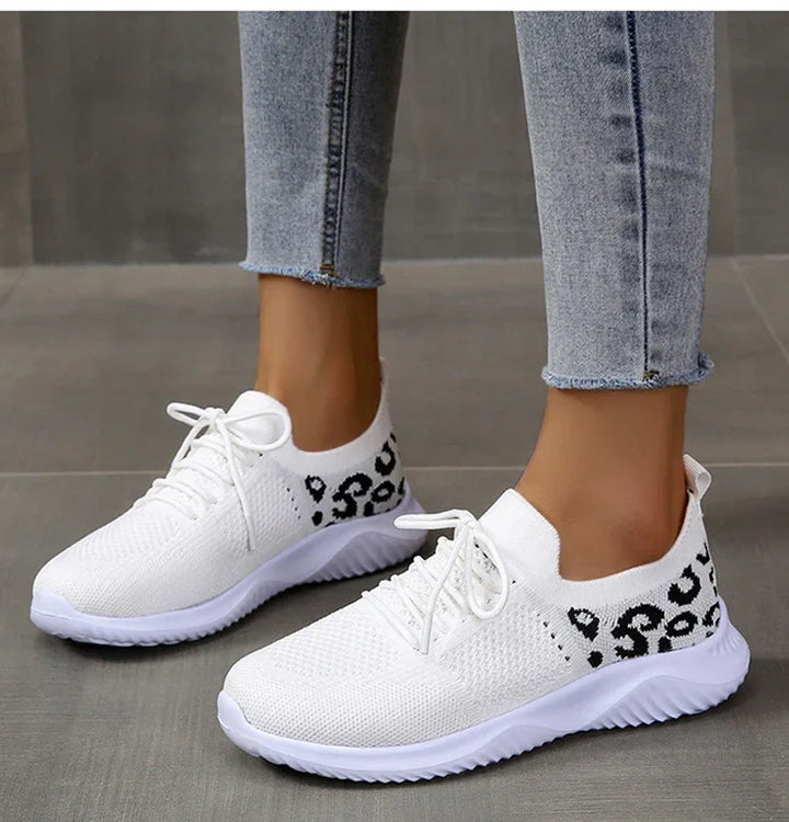 White knit sneakers with black leopard print detail worn with cropped light blue jeans on grey floor