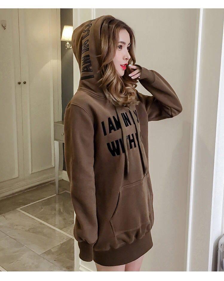 Woman wearing brown oversized hoodie with black text in a modern indoor setting