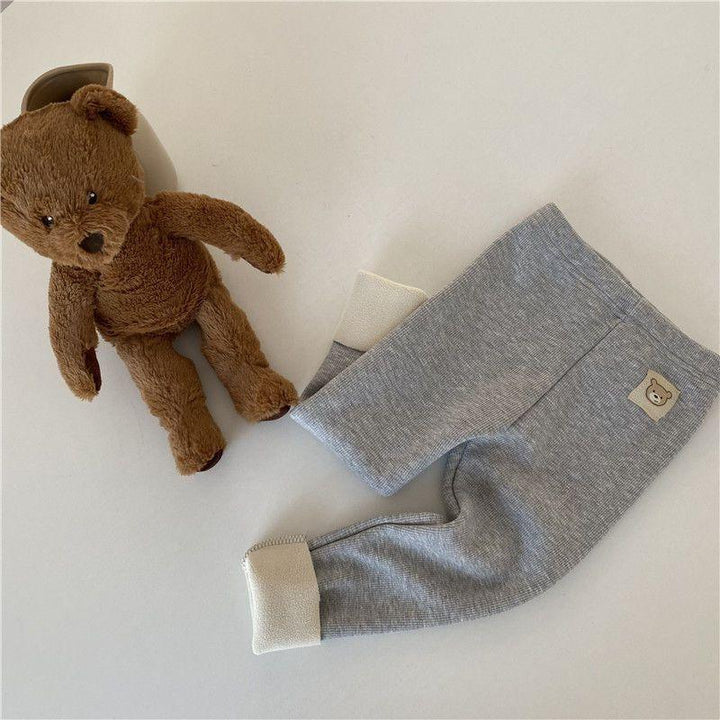 Brown teddy bear plush toy next to gray baby pants with bear patch on white background