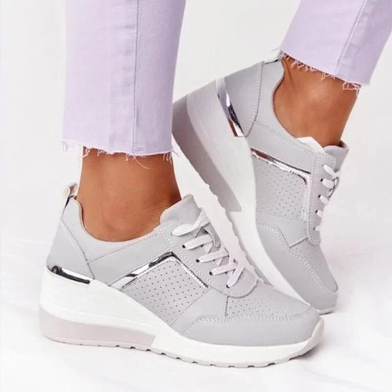 Light gray wedge sneakers with perforated design and metallic silver accents worn with frayed hem lavender pants