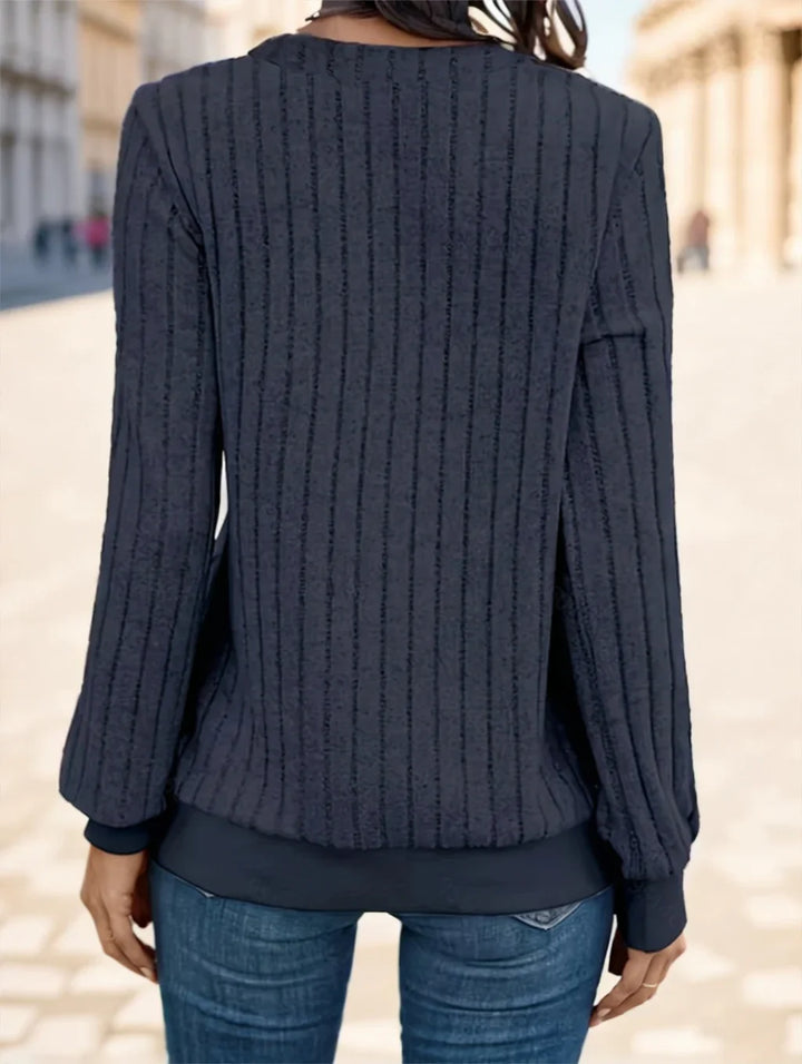 Back view of person wearing textured black long sleeve sweater and blue jeans on city street