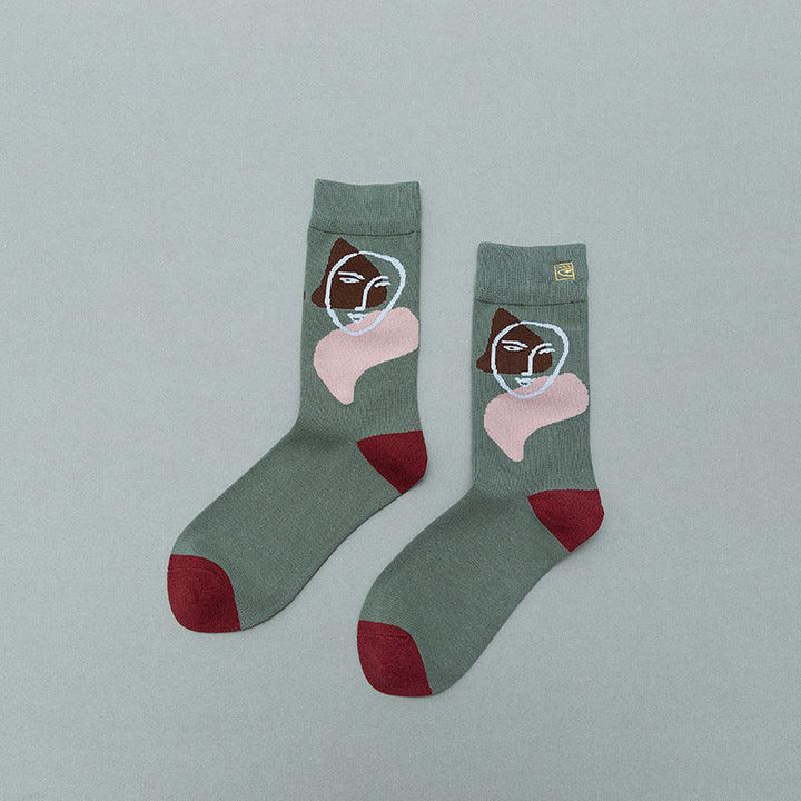 Green socks with abstract face and pink shapes, featuring red toes and heels on gray background