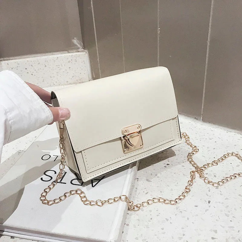 Hand holding small white leather handbag with gold chain strap on terrazzo countertop