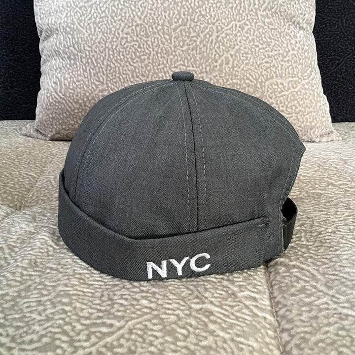 Dark gray NYC embroidered beanie cap on patterned beige couch with textured pillow