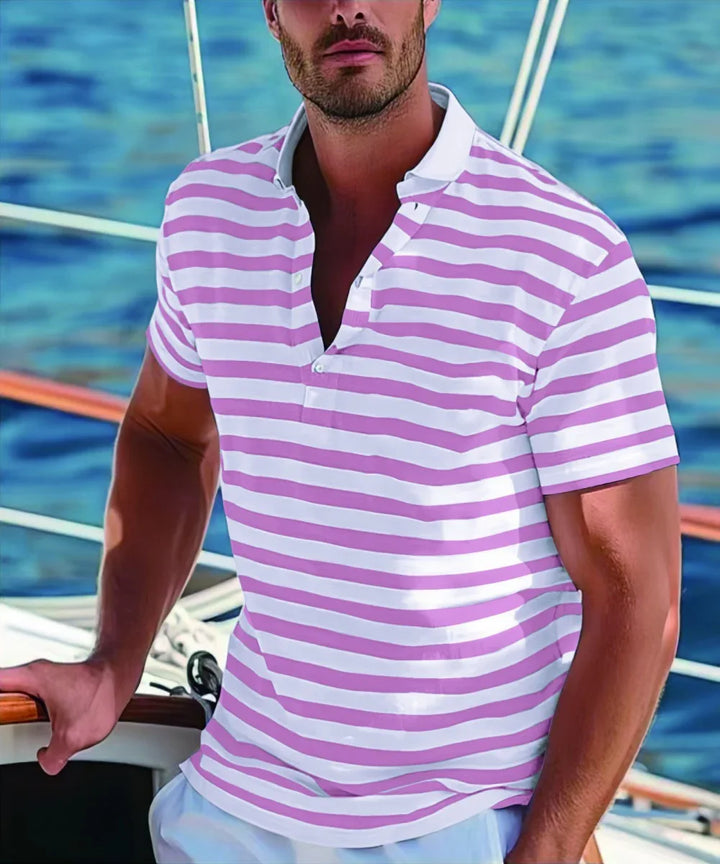 Man in pink and white striped polo shirt standing on a boat with ocean background