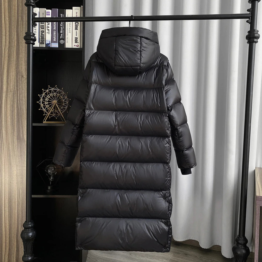 Long black padded winter coat with hood hanging on black metal rack in modern room