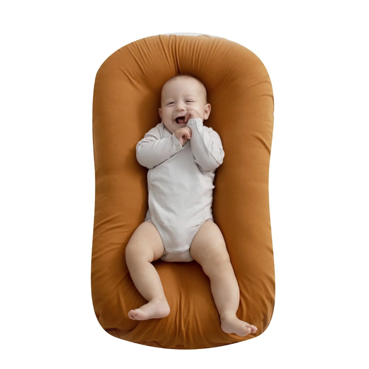 Smiling baby in white onesie lying on orange cushioned baby lounger against white background