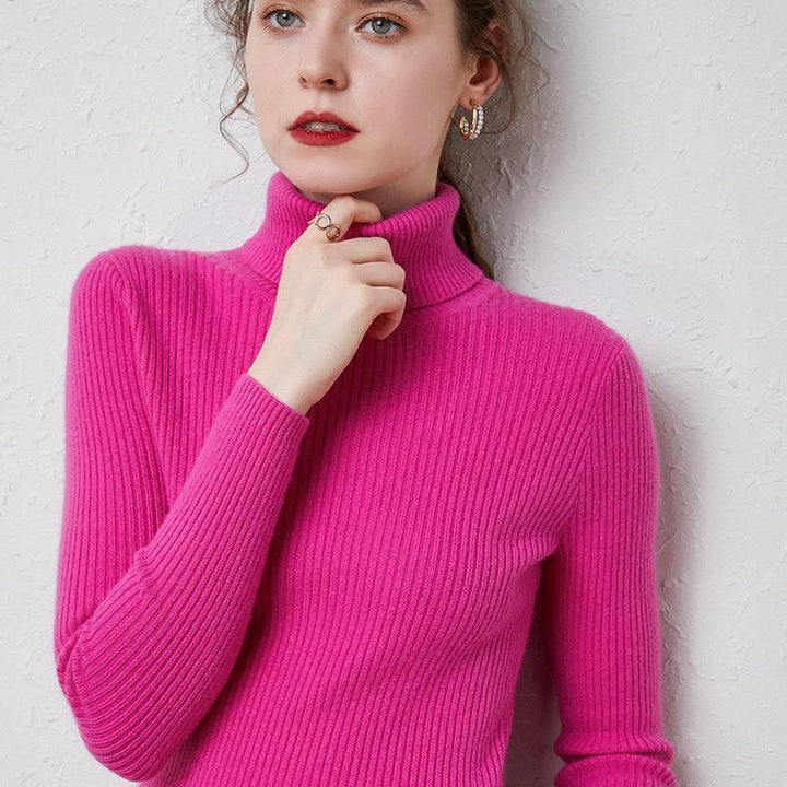 Woman wearing a bright pink ribbed turtleneck sweater with gold hoop earrings and a ring