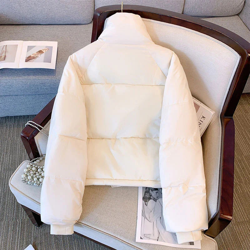 Cream white puffer jacket with high collar laid on beige armchair with magazine and pearl bag