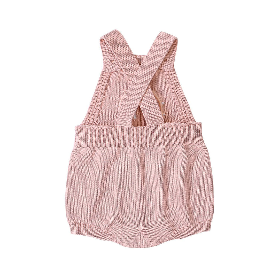 Pink knitted baby romper with crossed straps and ribbed waist on white background