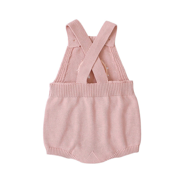 Pink knitted baby romper with crossed straps and ribbed waist on white background