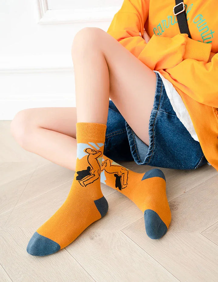Person wearing orange crew socks with artistic figure design, paired with denim shorts and orange sweatshirt