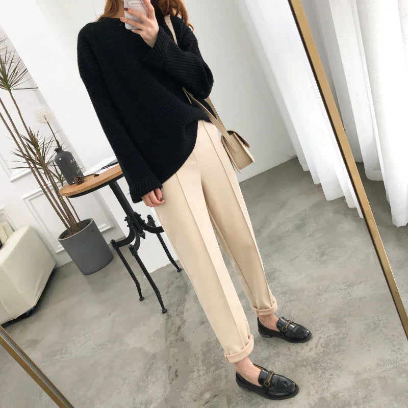 woman in black sweater beige pants and black loafers taking mirror selfie in modern minimal room