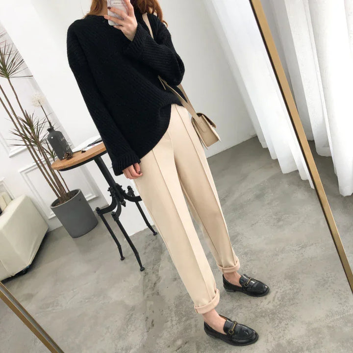 woman in black sweater beige pants and black loafers taking mirror selfie in modern minimal room