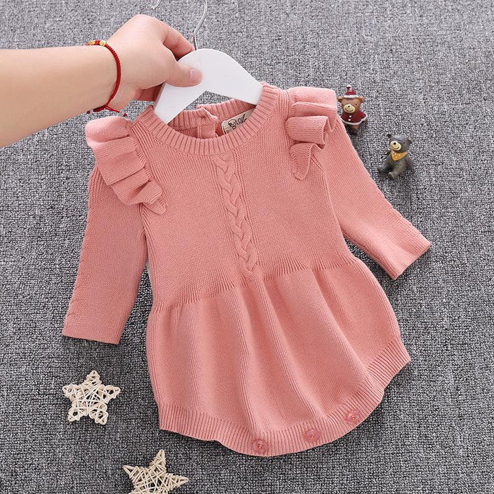 Pink knitted baby dress with ruffled shoulders and buttons, held over gray textured background