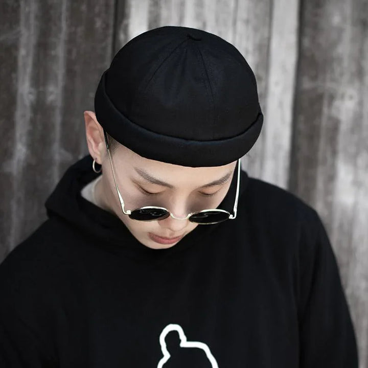 Young man in black hoodie and black beanie wearing round sunglasses looking down
