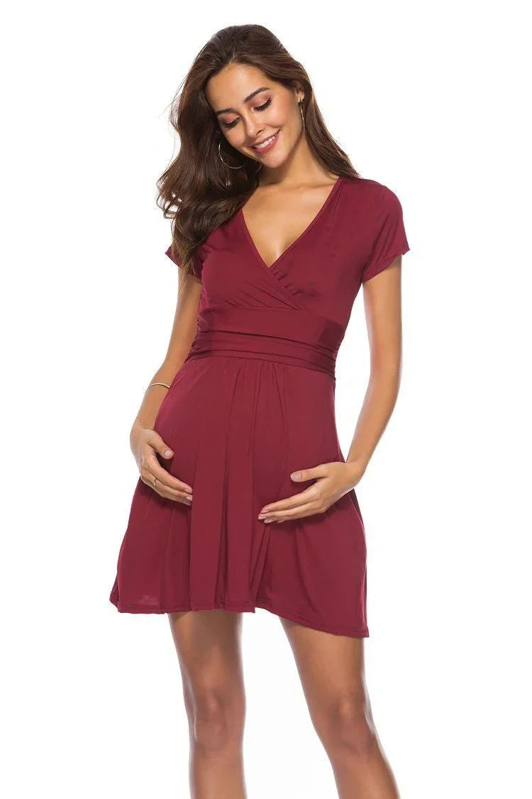 Smiling pregnant woman in a short-sleeve burgundy maternity dress holding her belly