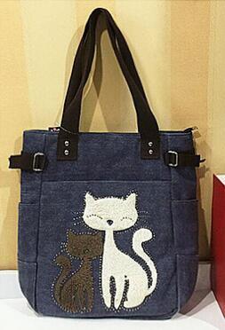 Dark blue tote bag with black straps featuring two embroidered cats, one white and one brown, on the front