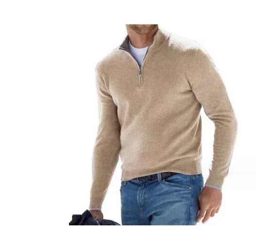 Man wearing beige quarter-zip sweater with blue jeans holding black jacket