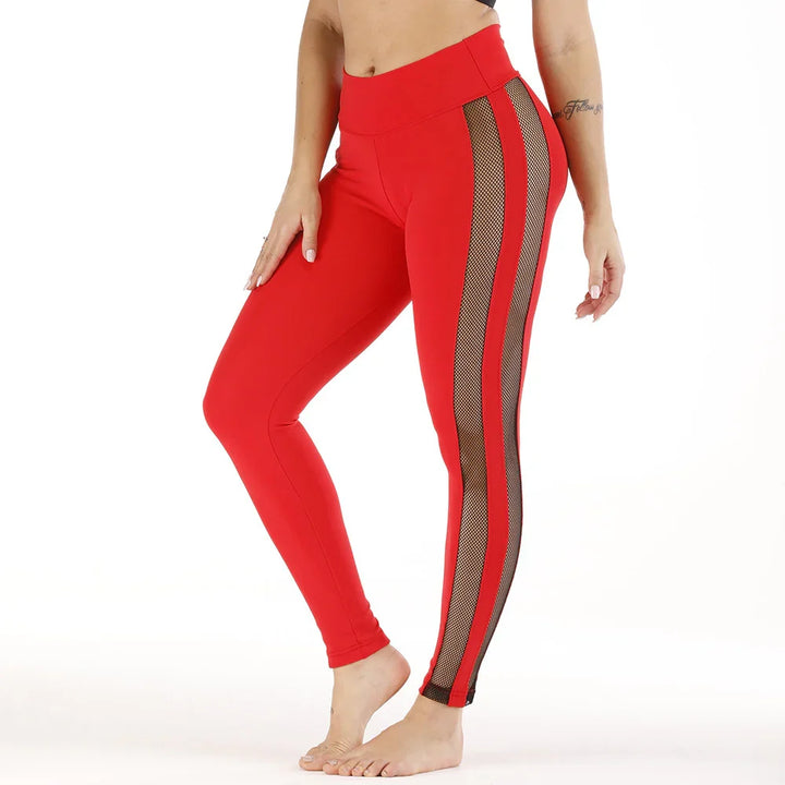 Woman wearing red high-waist leggings with black mesh side panels, barefoot on white background