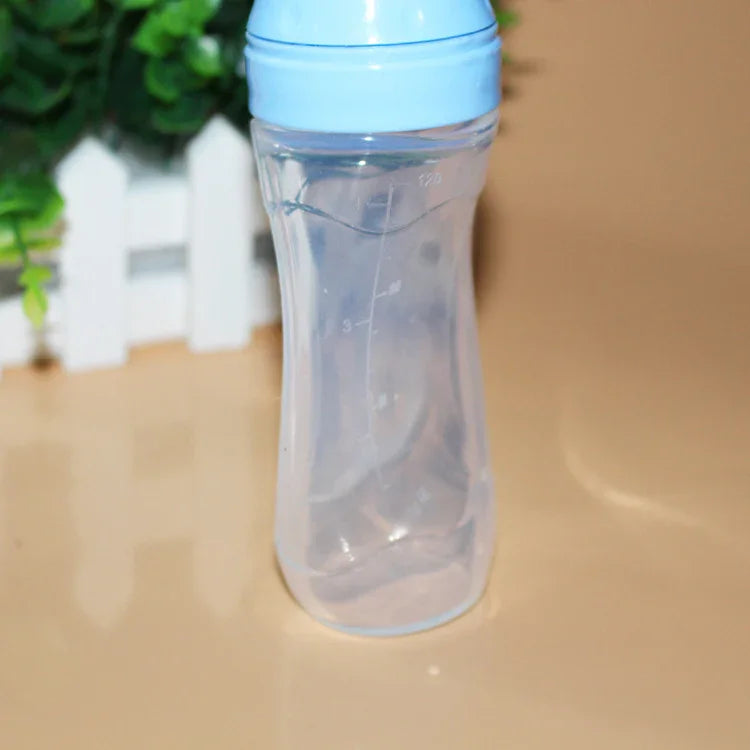 Clear baby feeding bottle with blue cap on beige surface and green plant background