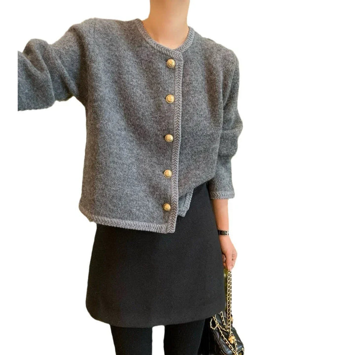 Woman wearing a gray buttoned cardigan with gold buttons and a black skirt, holding black handbag with gold chain