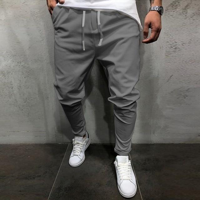 Man wearing gray jogger pants with white drawstrings and white sneakers against gray wall