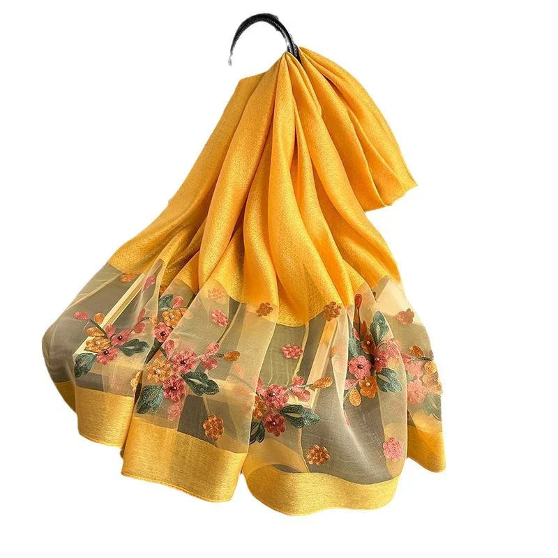 Yellow chiffon fabric with floral embroidery and sheer border, folded and draped on black hanger