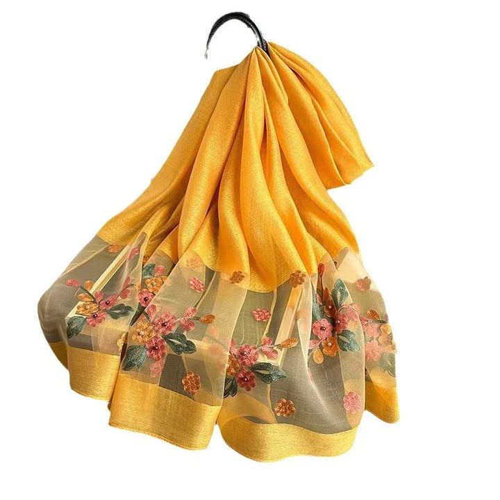 Yellow chiffon fabric with floral embroidery and sheer border, folded and draped on black hanger