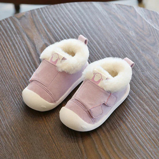 Pair of soft pink baby shoes with white fluffy lining on wooden surface